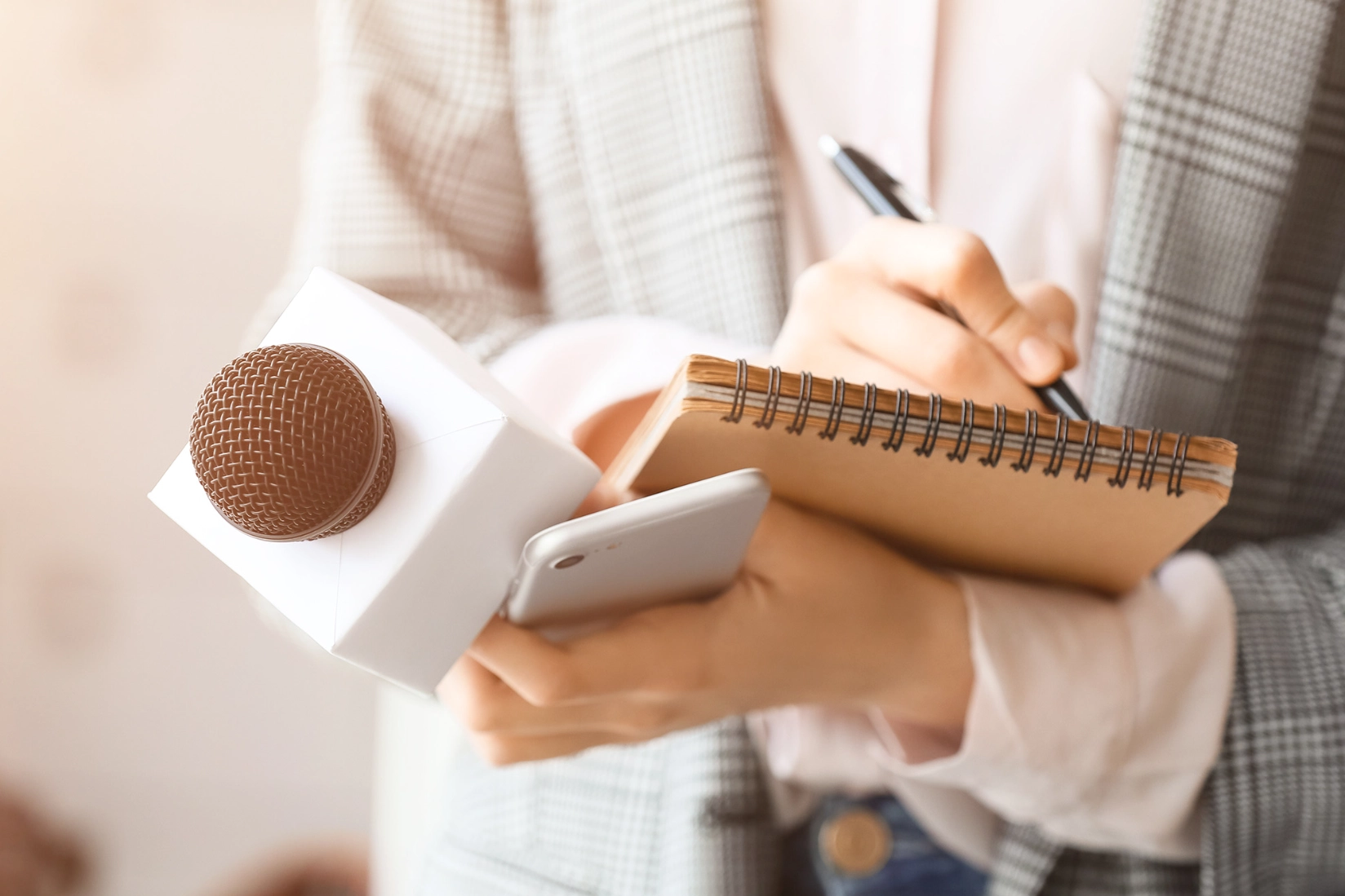 Close-up of a person holding a microphone while taking notes in a notebook.
